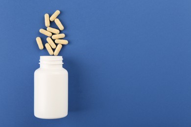 Photo of Bottle and vitamin capsules on blue background, top view. Space for text