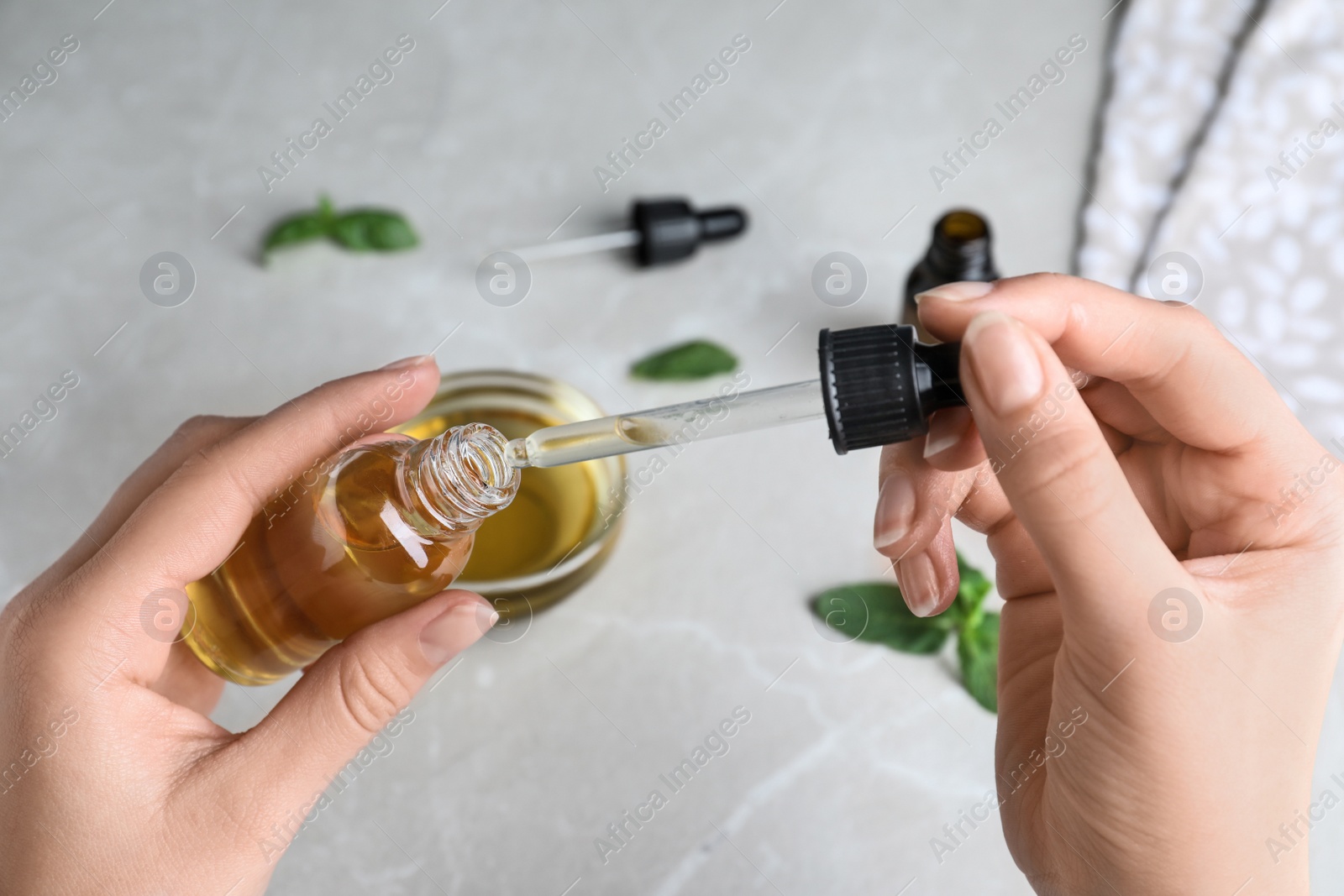 Photo of Woman with bottle of essential oil and pipette at table, closeup