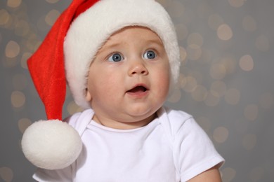 Photo of Cute baby in Santa hat against blurred lights. Christmas celebration