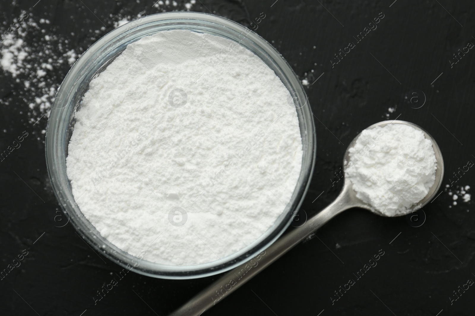 Photo of Baking powder in bowl and spoon on black textured table, top view