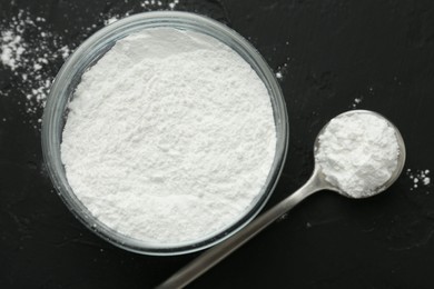 Baking powder in bowl and spoon on black textured table, top view