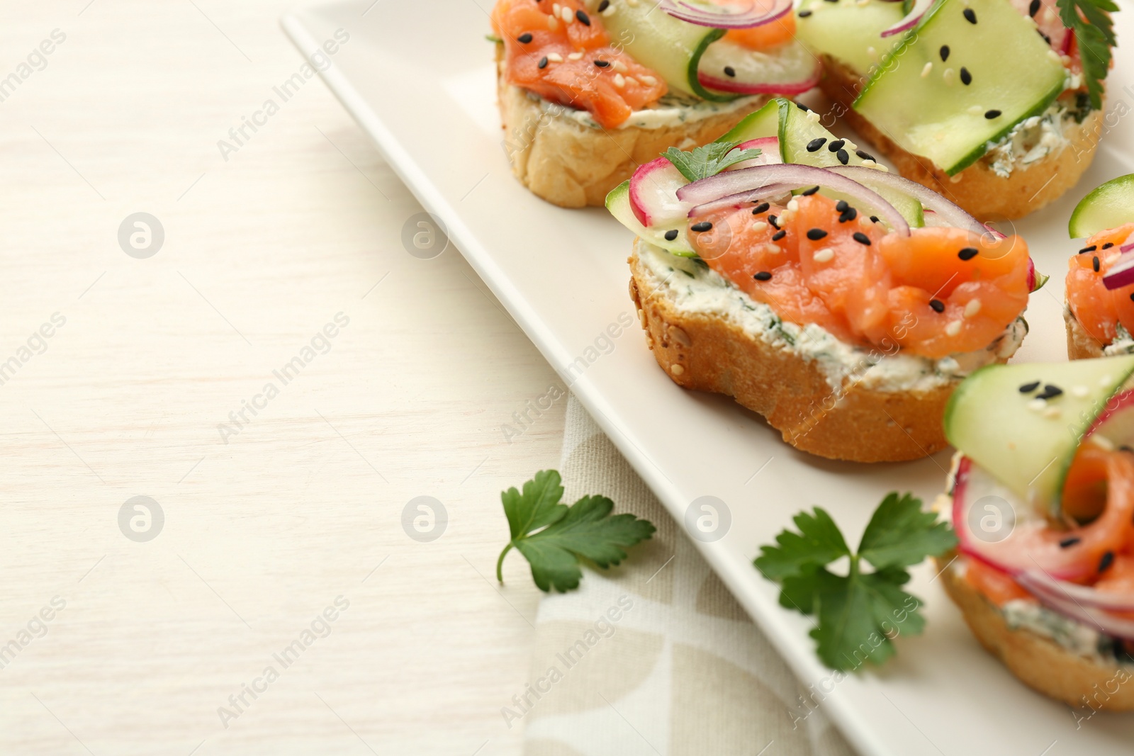 Photo of Tasty canapes with salmon served on white wooden table, closeup. Space for text