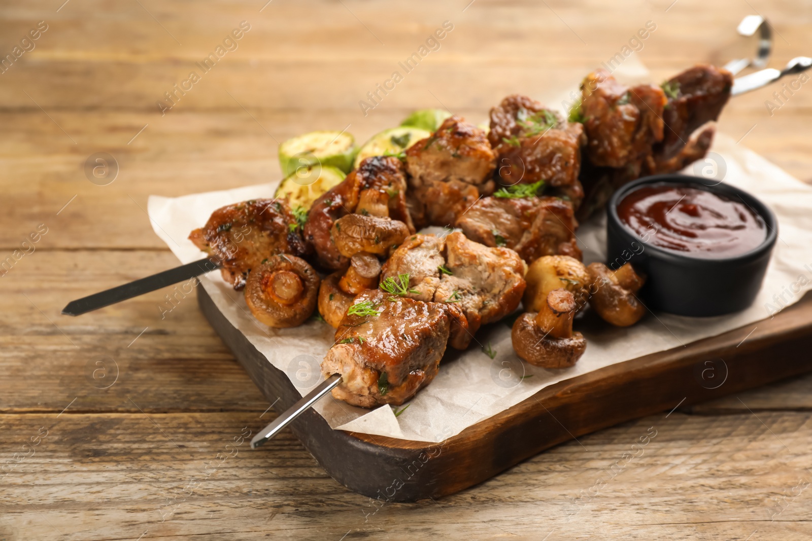 Photo of Metal skewers with delicious meat, ketchup and vegetables on wooden table