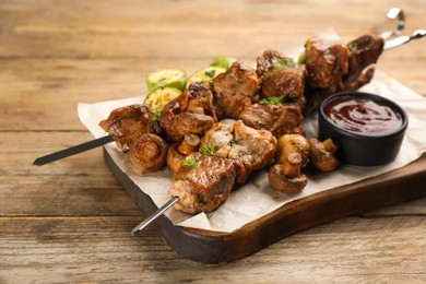 Metal skewers with delicious meat, ketchup and vegetables on wooden table