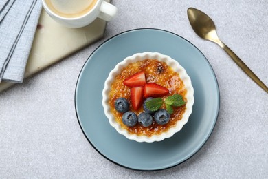 Photo of Delicious creme brulee with berries and mint in bowl served on grey textured table, flat lay