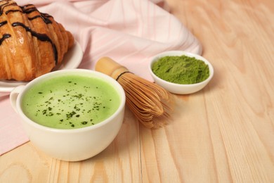 Photo of Cup of tasty matcha latte, bamboo whisk and green powder on wooden table, closeup