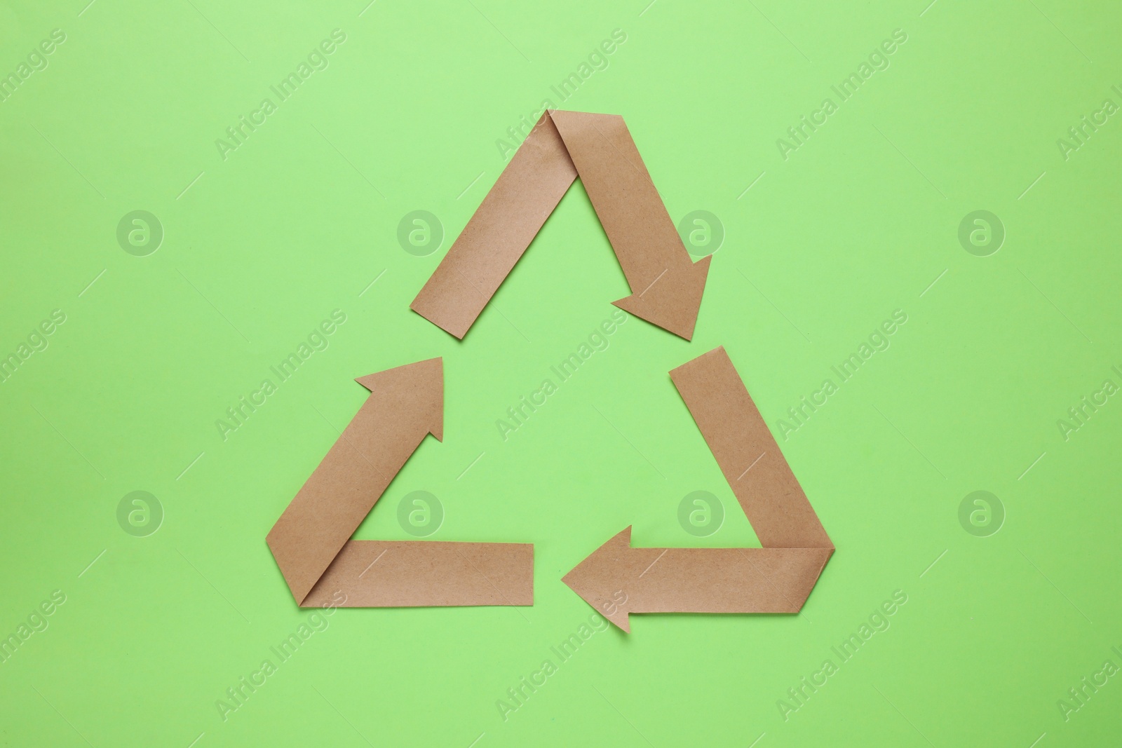 Photo of Recycling symbol cut out of paper on green background, top view