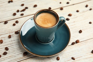 Photo of Cup of hot aromatic espresso and roasted beans on white wooden table