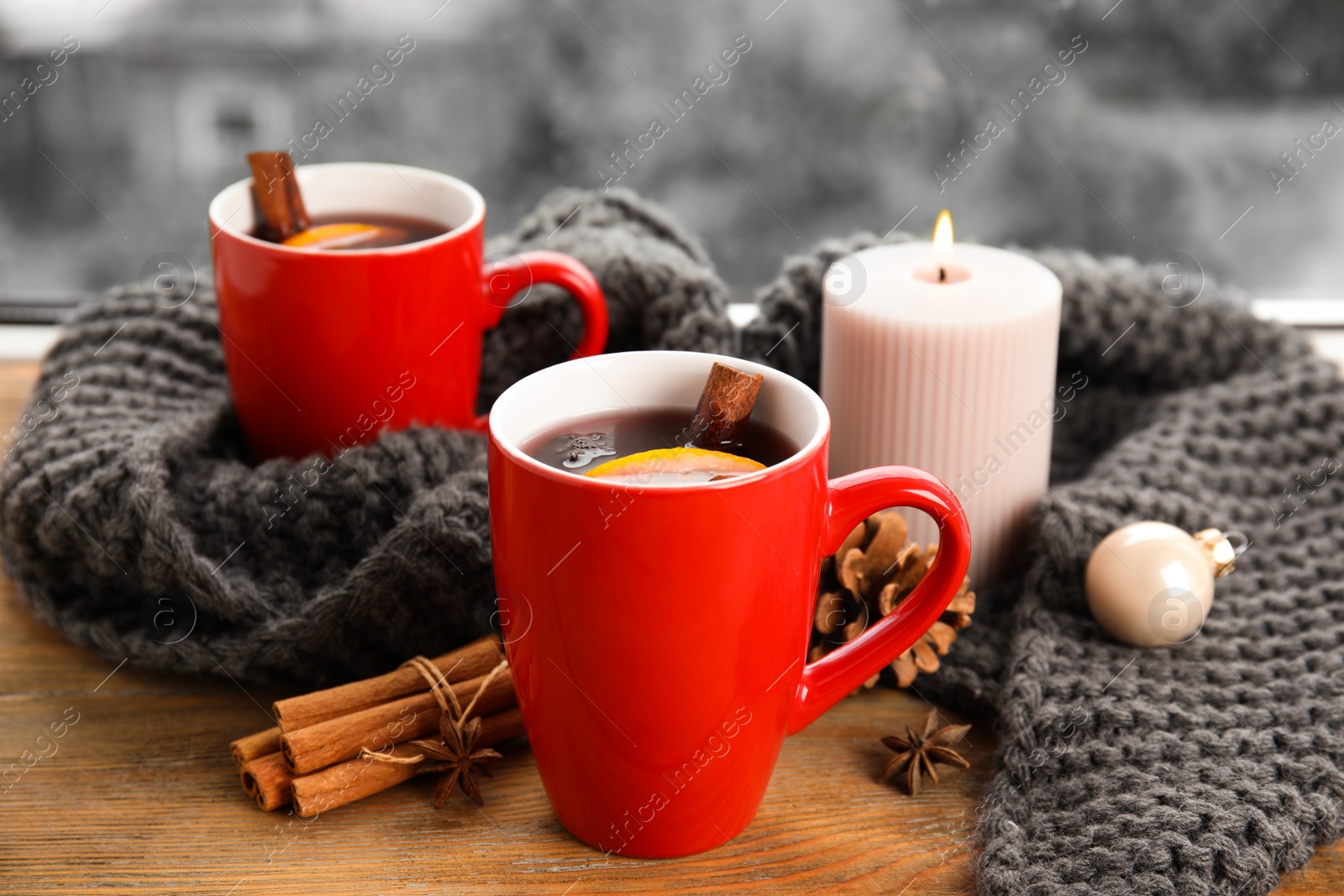 Photo of Cups of hot winter drink with scarf on window sill indoors