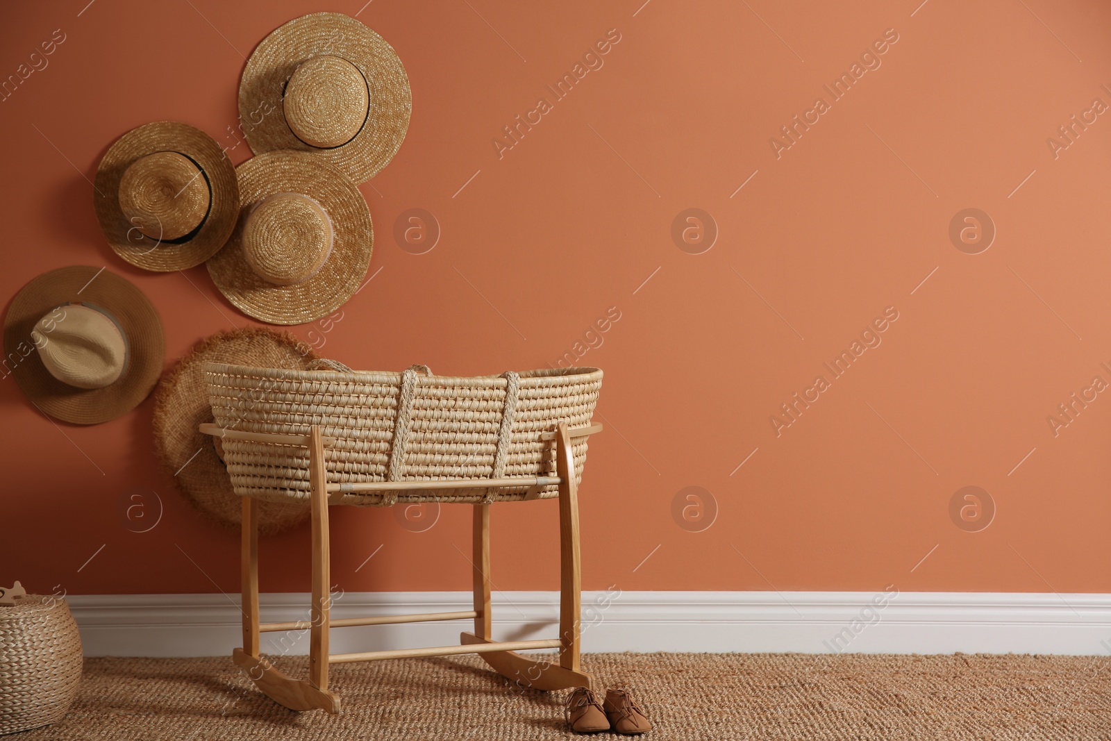 Photo of Wicker crib and straw hats on brown wall, space for text. Interior design