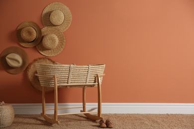 Wicker crib and straw hats on brown wall, space for text. Interior design