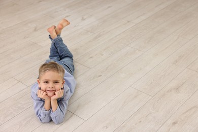 Photo of Cute little boy lying on warm floor at home, space for text. Heating system