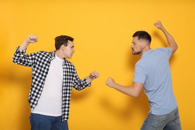 Photo of Two emotional men fighting on yellow background