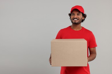 Photo of Happy young courier with parcel on grey background, space for text