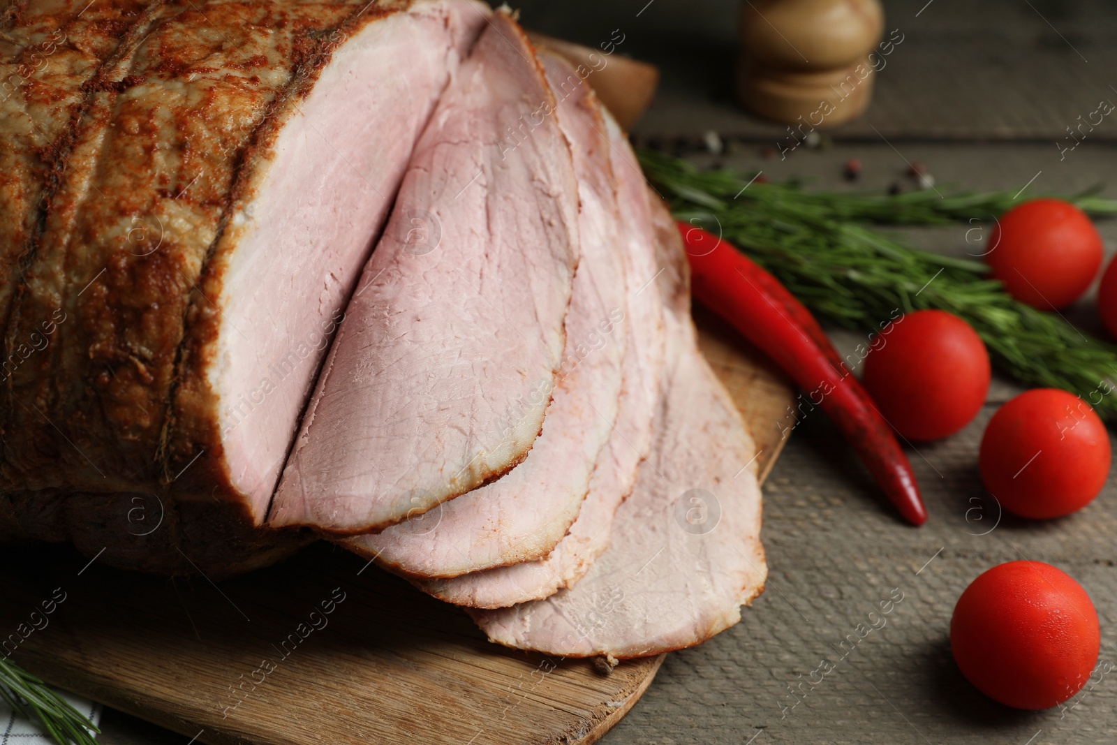 Photo of Delicious baked ham, tomatoes, chili pepper and rosemary on grey wooden table, closeup