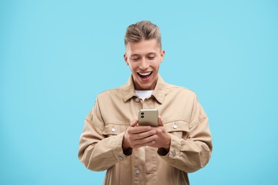 Emotional young man sending message via smartphone on light blue background