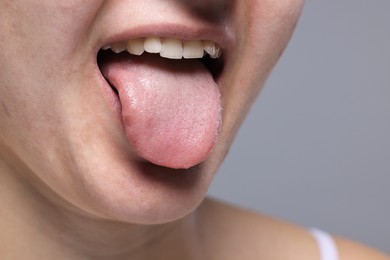 Woman showing her tongue on grey background, closeup. Space for text