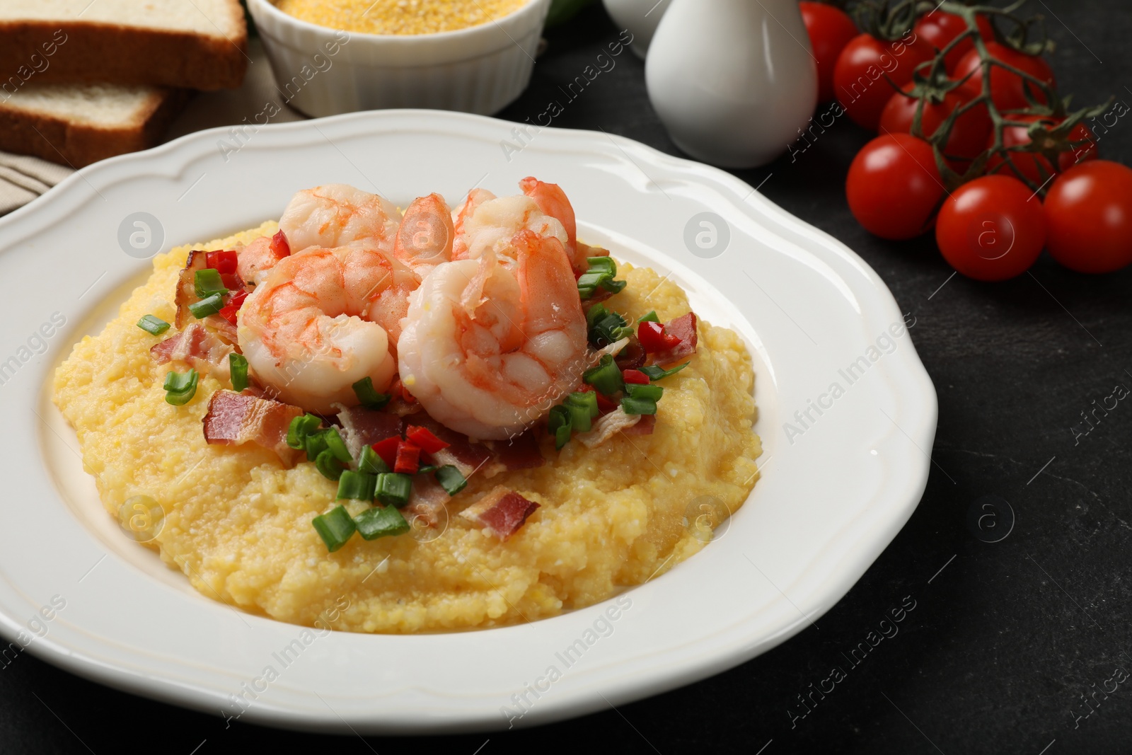 Photo of Plate with fresh tasty shrimps, bacon, grits, green onion and pepper on black table, closeup