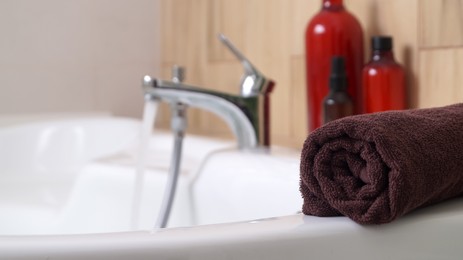 Rolled bath towel on tub in bathroom, space for text