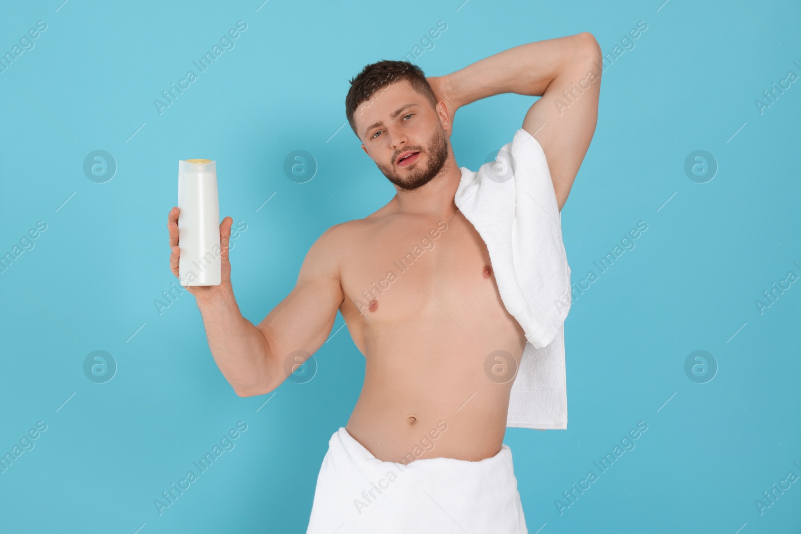 Photo of Shirtless young man holding bottle of shampoo on light blue background