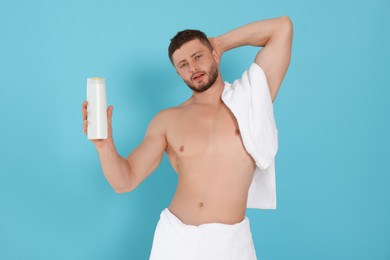 Shirtless young man holding bottle of shampoo on light blue background