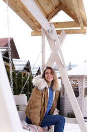 Photo of Young woman in warm clothes resting on outdoor swing. Winter vacation