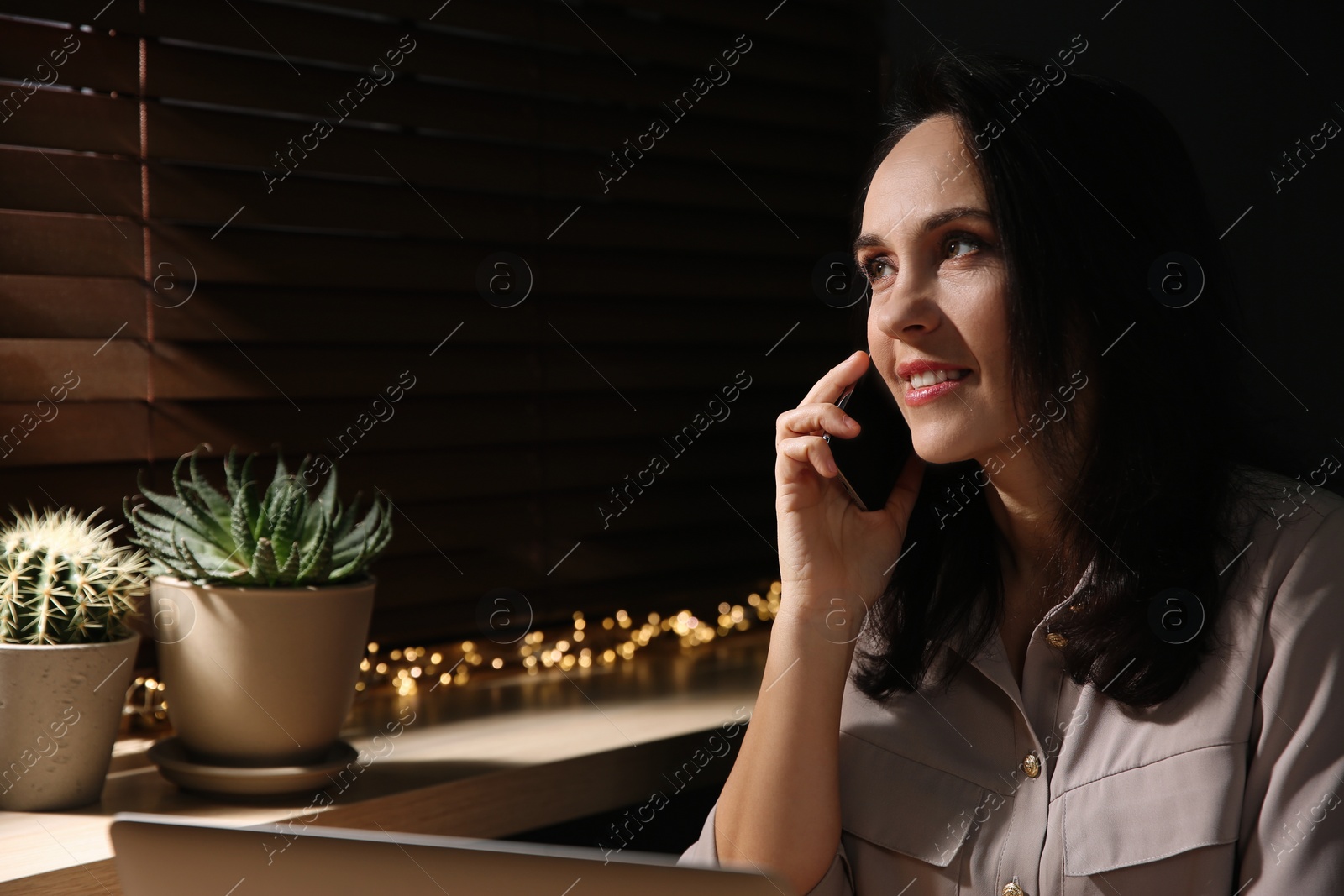 Photo of Beautiful mature woman talking on smartphone at home. Space for text