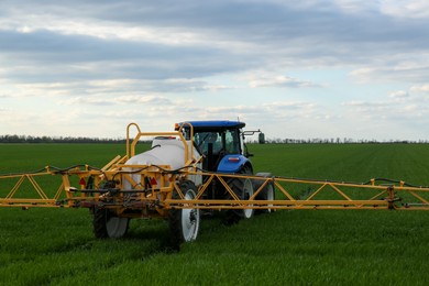 Photo of Tractor spraying pesticide in field on spring day. Agricultural industry