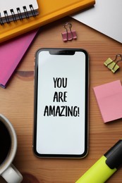 Photo of Smartphone with phrase You Are Amazing on screen and stationery against wooden background, flat lay