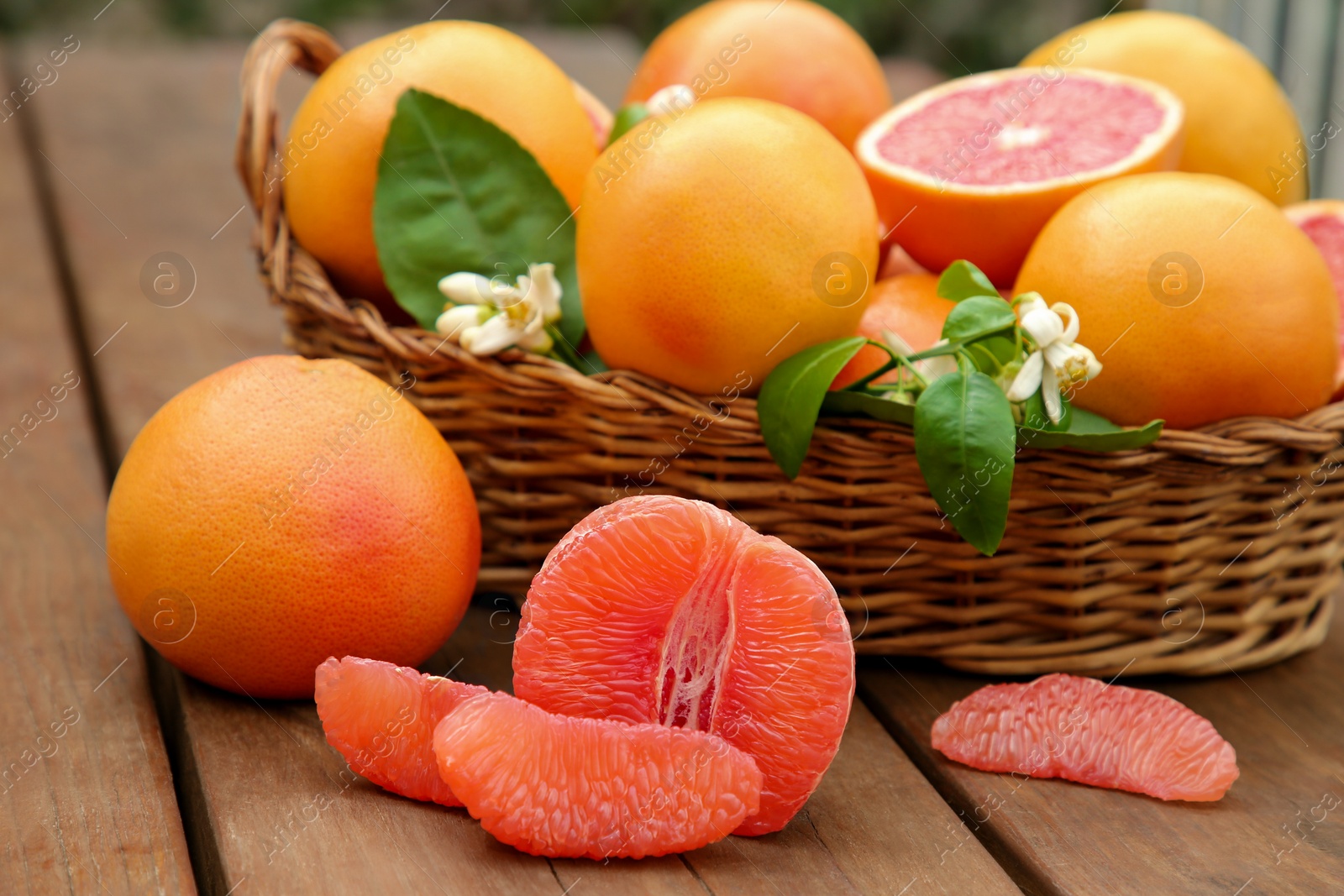 Photo of Wicker basket with fresh grapefruits and green leaves on wooden table, closeup