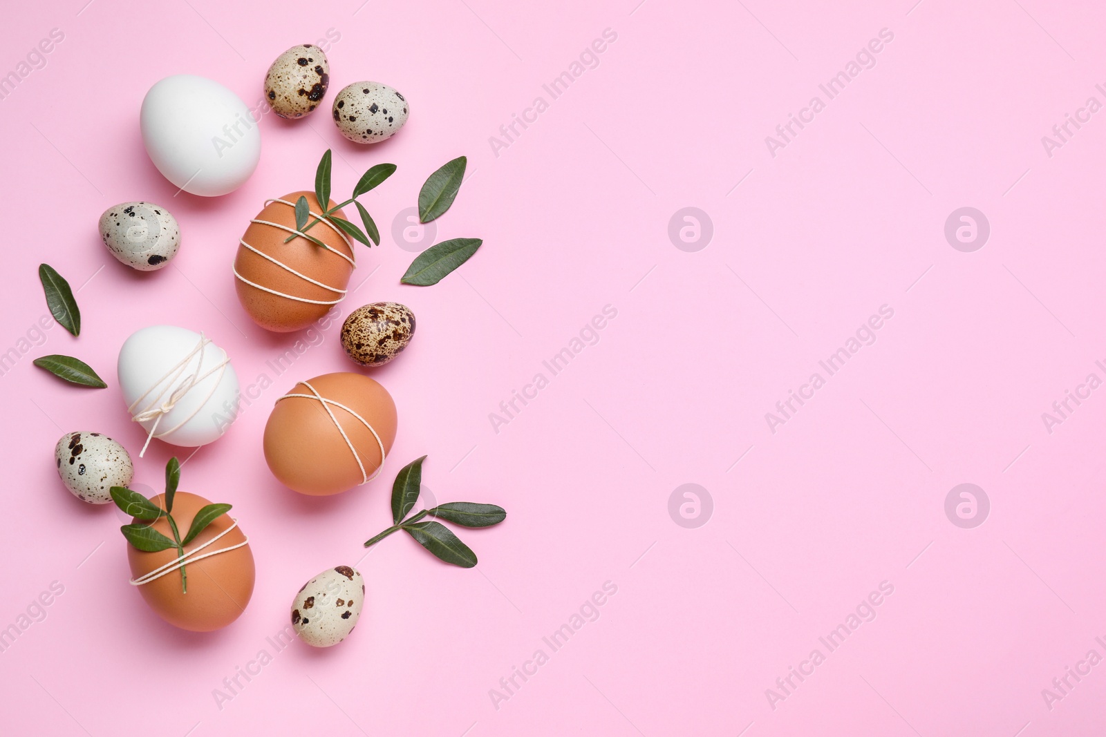 Photo of Beautifully decorated Easter eggs and green leaves on pink background, flat lay. Space for text