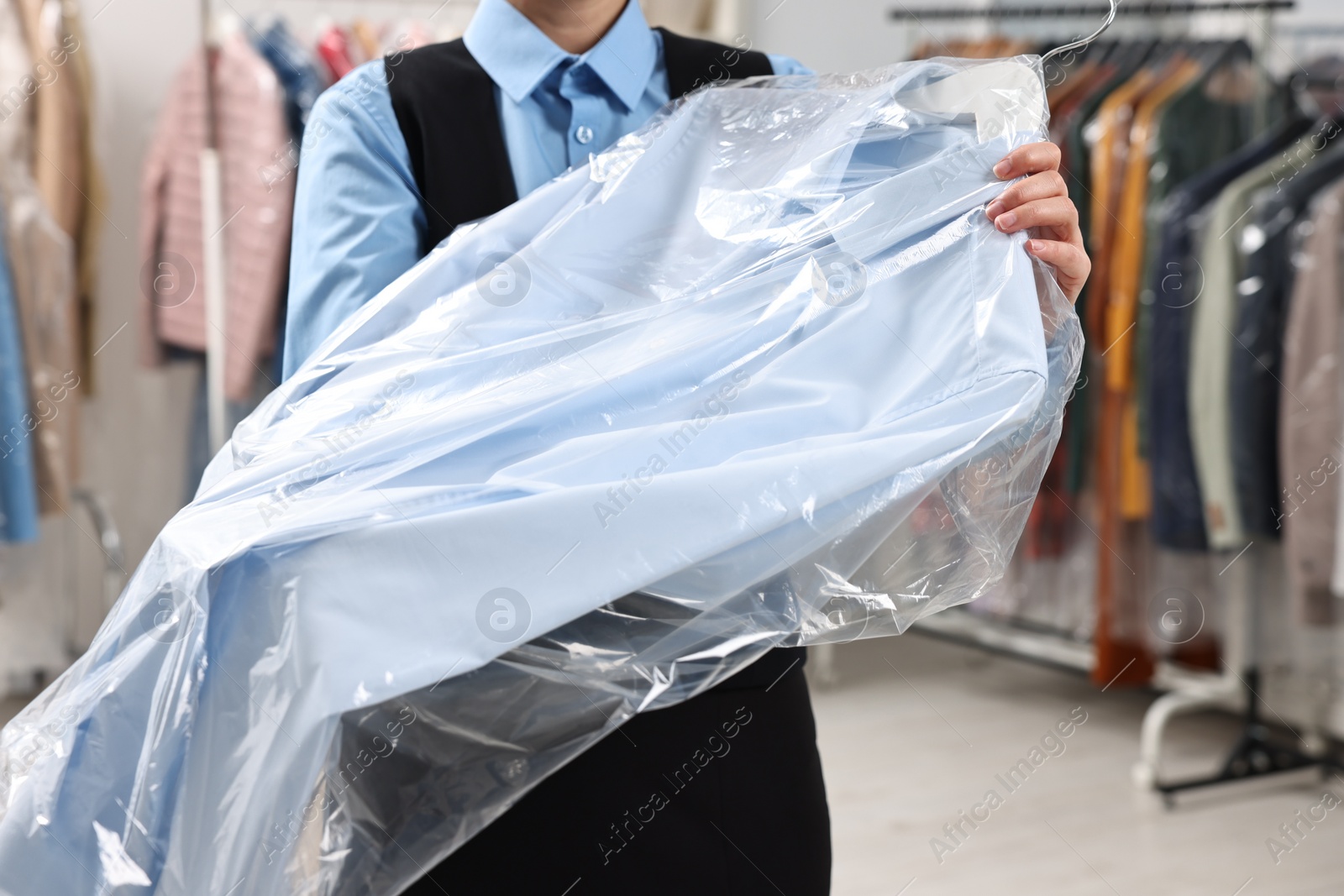 Photo of Dry-cleaning service. Woman holding shirt in plastic bag indoors, closeup