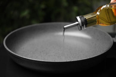 Photo of Woman pouring cooking oil from bottle into frying pan, closeup