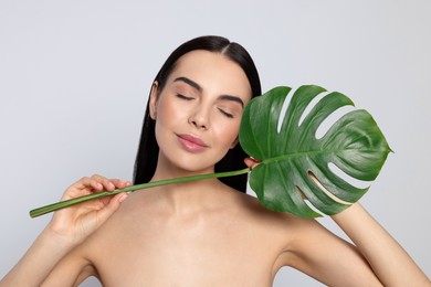Woman holding leaf of monstera on light grey background. Spa treatment