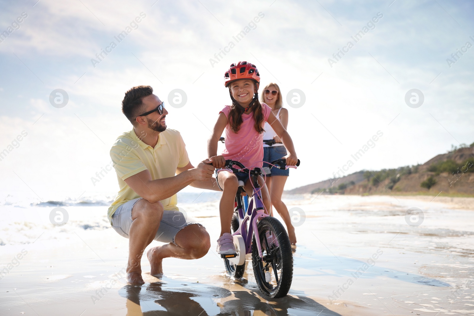 Photo of Happy parents teaching children to ride bicycles on sandy beach near sea