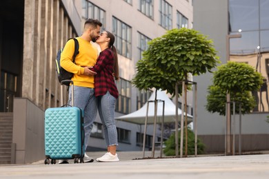 Photo of Long-distance relationship. Beautiful couple with luggage kissing outdoors, low angle view
