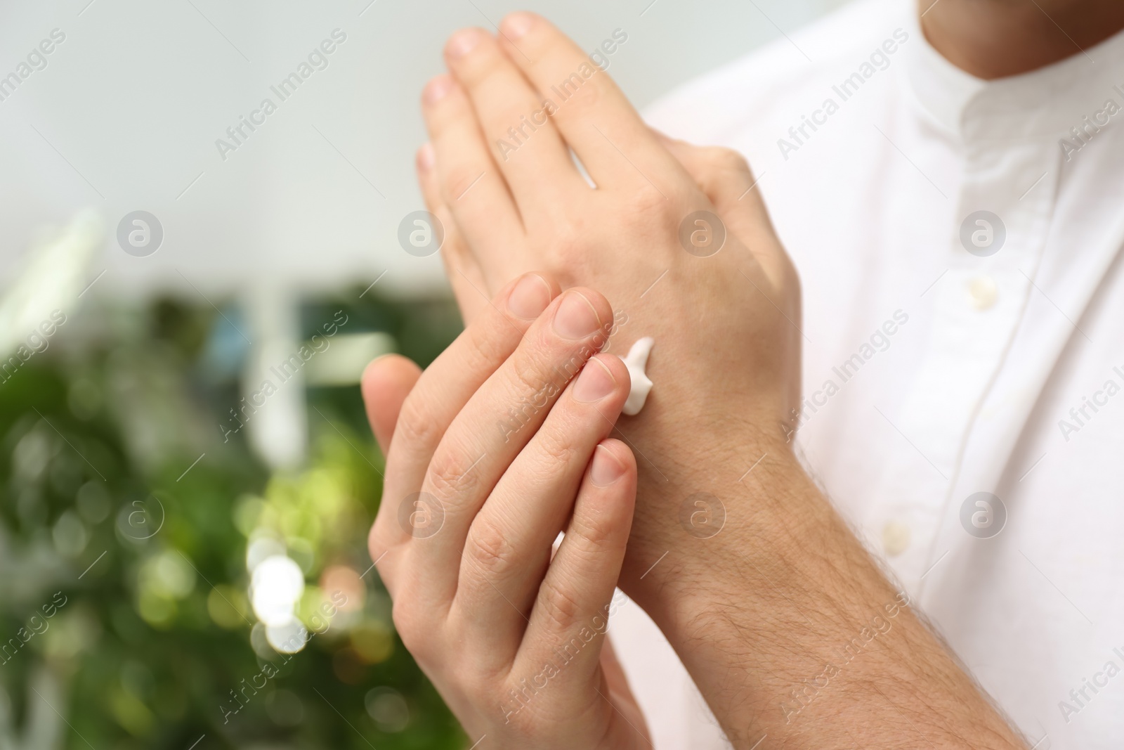 Photo of Man applying moisturizing cream onto hand on blurred background, closeup