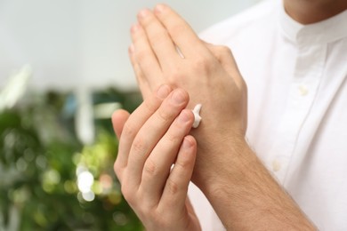 Photo of Man applying moisturizing cream onto hand on blurred background, closeup