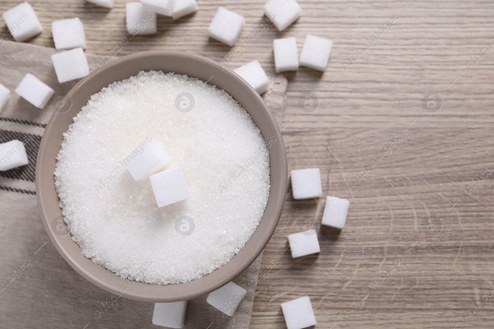 Photo of Different types of white sugar in bowl on wooden table, top view. Space for text