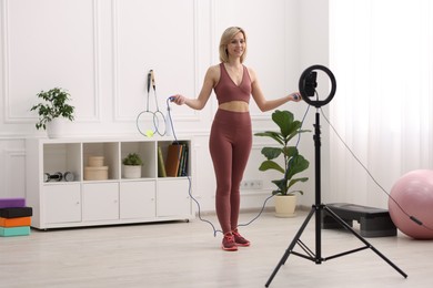 Photo of Smiling sports blogger holding skipping rope while streaming online fitness lesson at home
