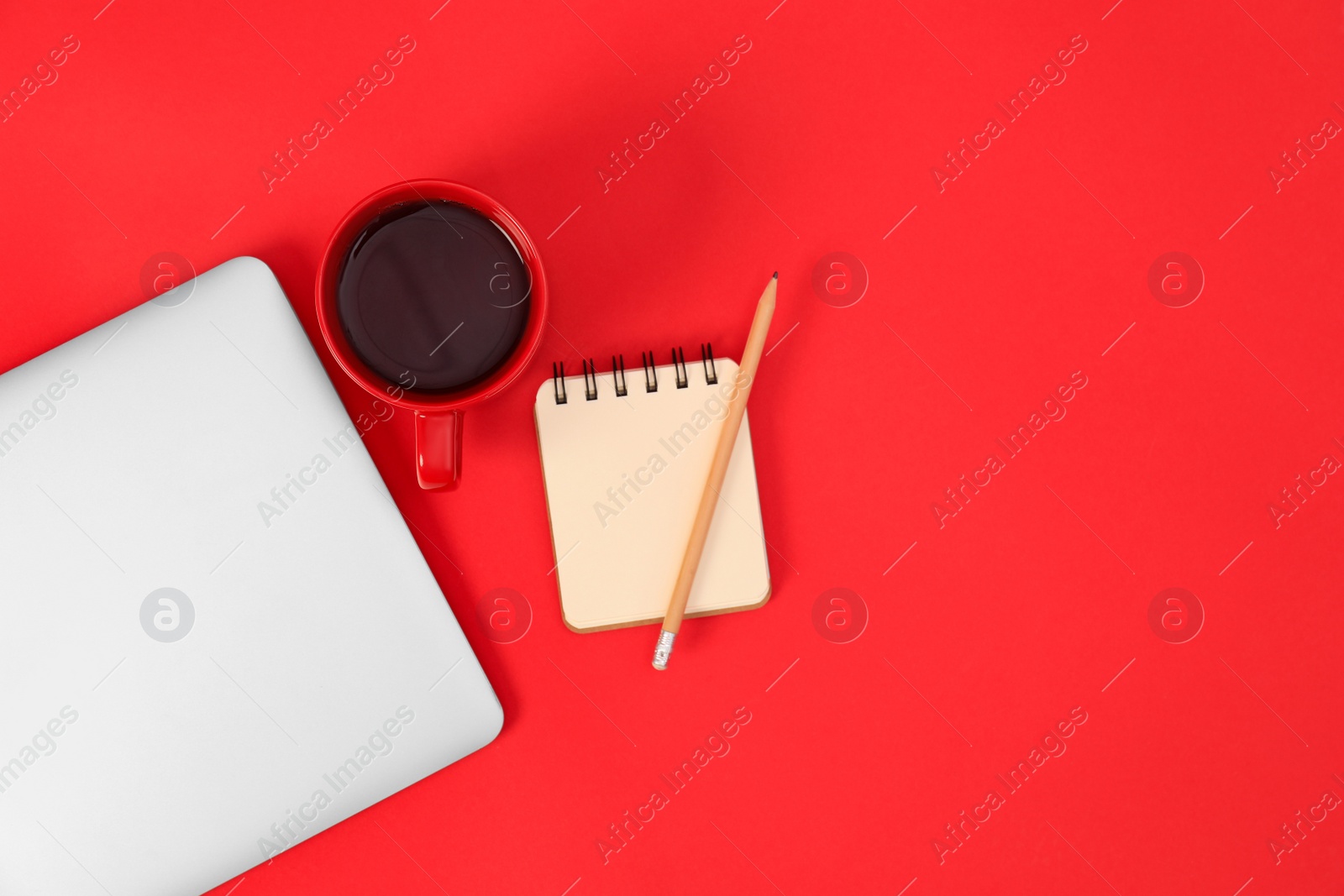 Photo of Modern laptop with cup of coffee and office tools on red background, top view. Space for text