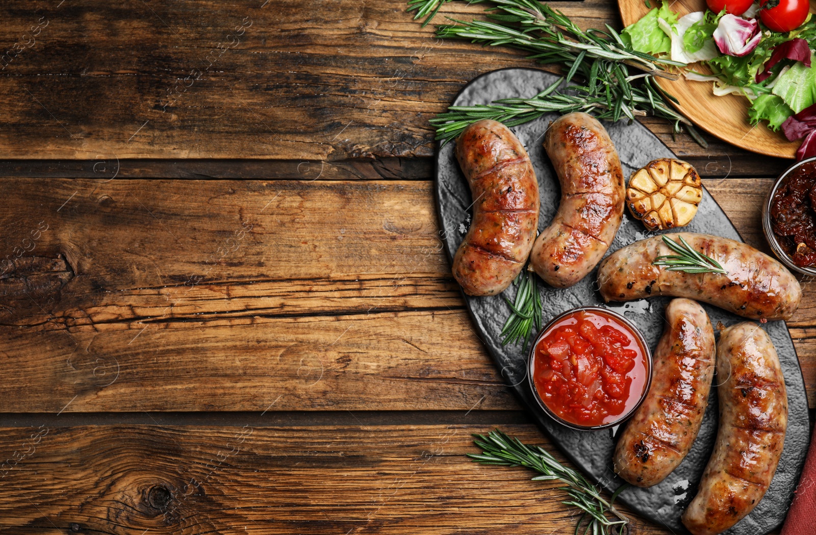 Photo of Tasty grilled sausages served on wooden table, flat lay. Space for text