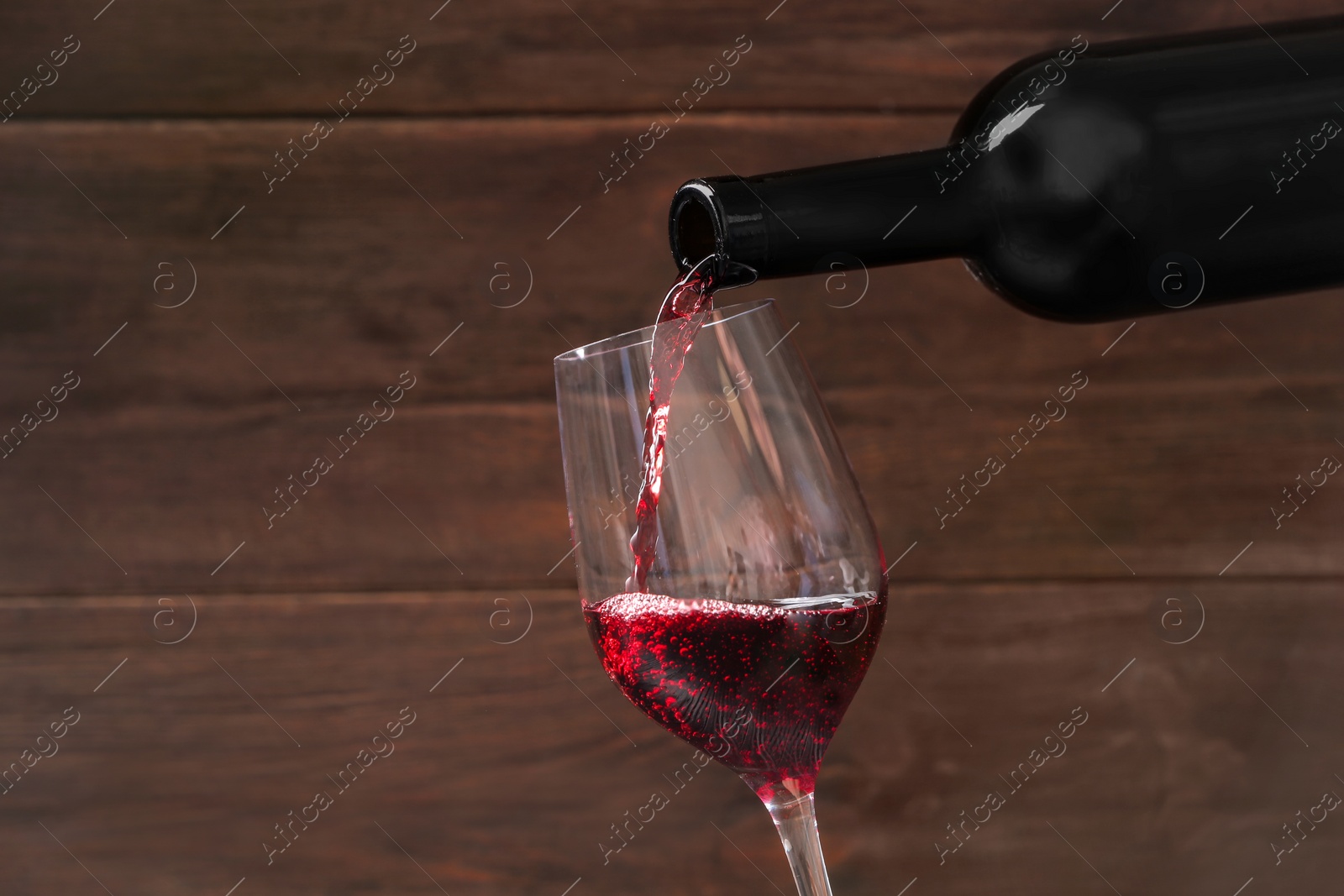 Photo of Pouring delicious red wine into glass on wooden background