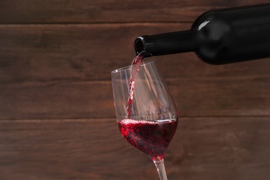 Pouring delicious red wine into glass on wooden background