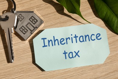 Photo of Inheritance Tax. Card, key with key chain in shape of house on wooden table, closeup
