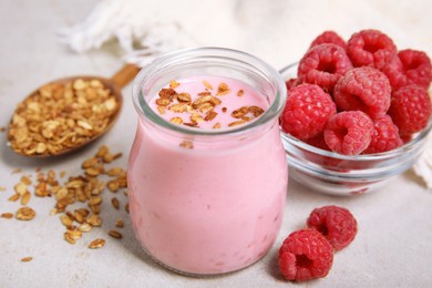 Photo of Tasty raspberry smoothie with granola in glass jar and fresh berries on light table, closeup