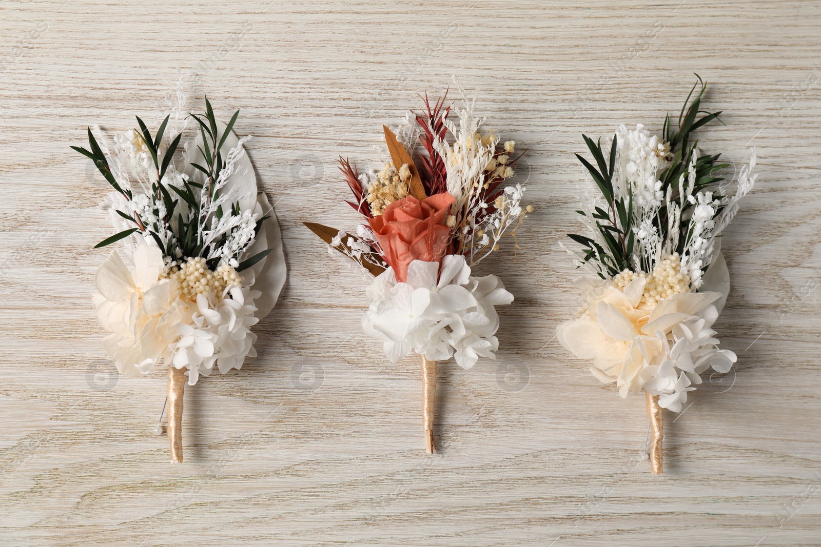 Photo of Stylish boutonnieres on white wooden table, flat lay
