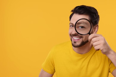 Happy man looking through magnifier glass on yellow background. Space for text