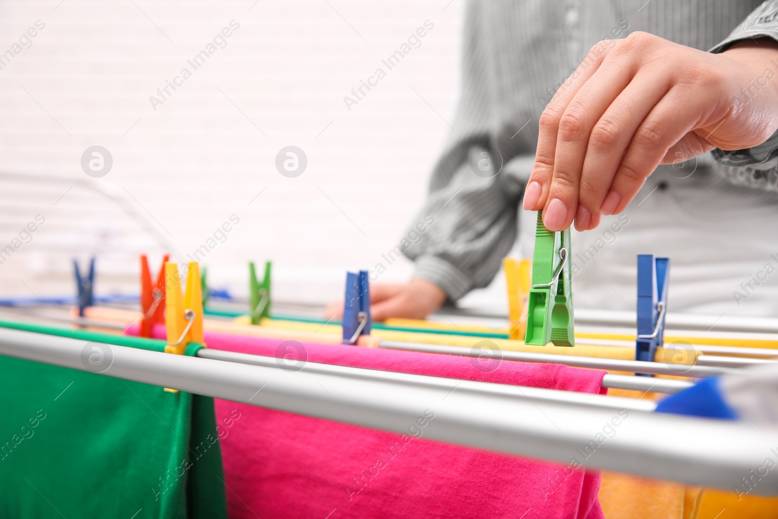 Photo of Young woman hanging clean laundry on drying rack, closeup