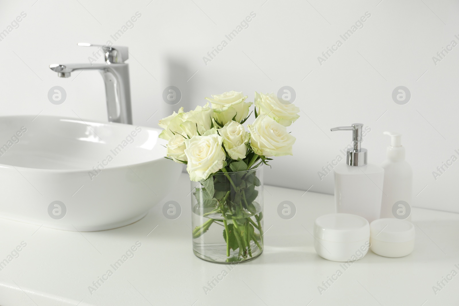 Photo of Bouquet of beautiful roses in vase and bath accessories near sink in bathroom